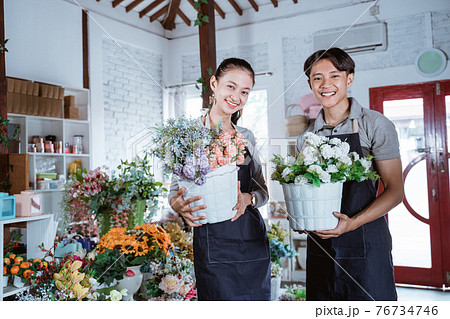 happy young couple wearing apron holding bucket flower smiling happy young couple wearing apron holding bucket flower smiling 76734746