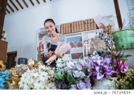 woman working in flower shop wearing apron preparing order 76734834