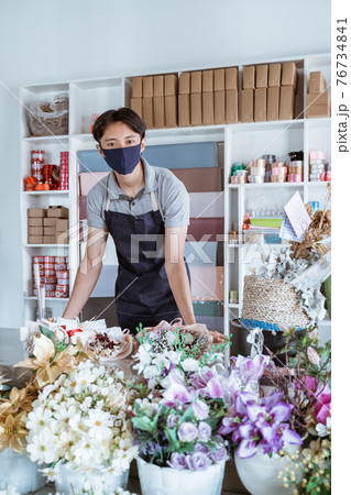 florist man wearing face mask standing behind a flower bouquet florist man wearing face mask standing behind a flower bouquet 76734841
