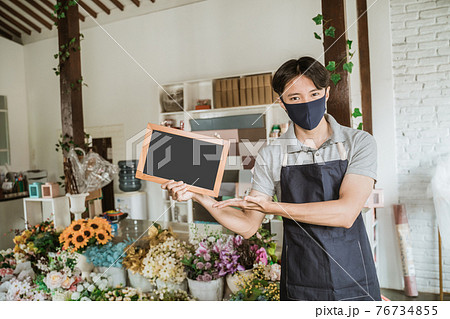 man using face mask florist standing holding small blank blackboard fresh flowers in his floral shop man using face mask florist standing holding small blank blackboard fresh flowers in his floral shop 76734855