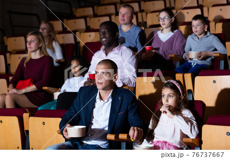 Dad and daughter carefully watch a movie in cinema hall 76737667