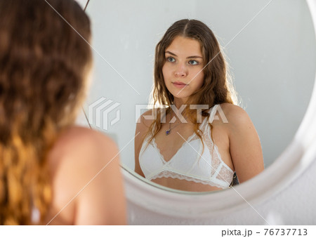Young woman with brown wavy hair looking at mirror 76737713