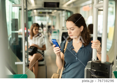 Positive woman reading from mobile phone screen in the cabin of bus or tram Positive woman reading from mobile phone screen in the cabin of bus or tram 76738296