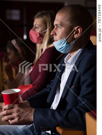close up of european man in mask sitting at film in cinema auditorium close up of european man in mask sitting at film in cinema auditorium 76738449