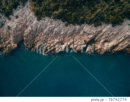 Top view of the coastline with cliff, turquoise water, rocks, foam, waves and trees. 76742774