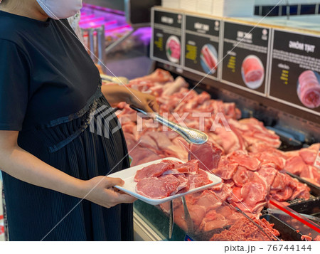 Pregnant woman wearing mask and buying pork meat Pregnant woman wearing mask and buying pork meat 76744144