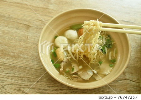 Chinese egg yellow noodles topping slice boiled pork and ball with soup pickonh by chopsticks in bowl 76747257
