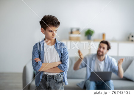 Furious father shouting at offended son while sitting with laptop computer on sofa at home, selective focus 76748455