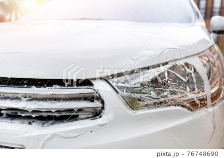 Close-up detail manual car wash with high pressure water equipment pump and soapy sponge at home backyard outdoor summer day. Vehicle covered by foam shampoo chemical detergents carwash self service Close-up detail manual car wash with high pressure water equipment pump and soapy sponge at home backyard outdoor summer day. Vehicle covered by foam shampoo chemical detergents carwash self service 76748690