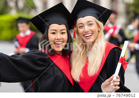 Happy multiracial young ladies in graduation clothes taking selfie Happy multiracial young ladies in graduation clothes taking selfie 76749012