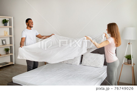 Cheerful multiracial couple making bed in morning, having fun at home Cheerful multiracial couple making bed in morning, having fun at home 76749026