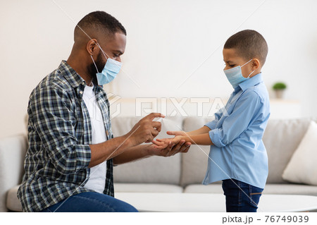 African American Dad Spraying Hand Sanitizer Disinfecting Son's Hands Indoor 76749039