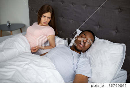 Young black guy snoring and bothering his angry sleepless wife in bed at home Young black guy snoring and bothering his angry sleepless wife in bed at home 76749065
