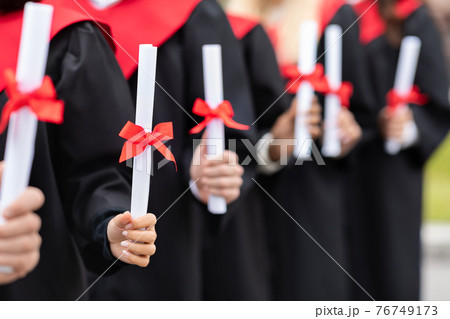 Unrecognizable multiracial group of graduates holding diplomas 76749173