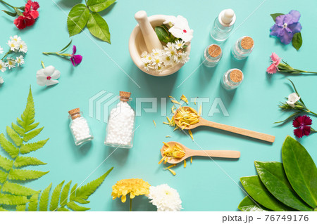 Homeopathic globules bottle with herb, flower, spoon and motar on green backgound. Homeopathy alternative medicine concept. Top view. 76749176