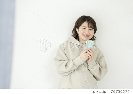 ヘッドホンをしてスマホを持つ笑顔の若い女性 ヘッドホンをしてスマホを持つ笑顔の若い女性 76750574