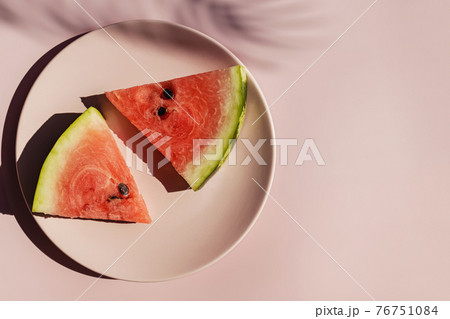 Fresh red watermelon slices on pink plate and tropical leaf shadow. Fresh red watermelon slices on pink plate and tropical leaf shadow. 76751084