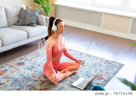 Young woman in white headphones during online yoga practice - meditation. Young woman in white headphones during online yoga practice - meditation. 76754146