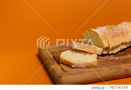 Sliced bread baguette on a wooden cutting board on a terracote color background. Close-up high quality photo. 76754739