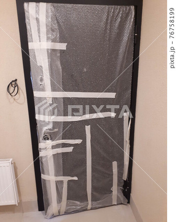 The new iron door is sealed with tape and foil to protect it from damage during repairs in a new building The new iron door is sealed with tape and foil to protect it from damage during repairs in a new building 76758199