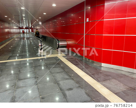 Large red modern long bright underground walkway between metro stations with travel walkers and escalators for quick passage of passengers Large red modern long bright underground walkway between metro stations with travel walkers and escalators for quick passage of passengers 76758214