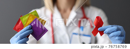 Doctor in protective gloves holding red ribbon and condoms closeup 76758769