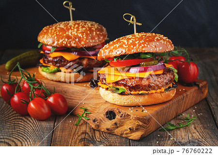 Two delicious homemade burgers of beef, cheese and vegetables on an old wooden table. Fat unhealthy food close-up Two delicious homemade burgers of beef, cheese and vegetables on an old wooden table. Fat unhealthy food close-up 76760222