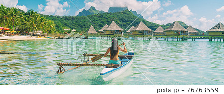 Bora Bora travel vacation iconic photo. Outrigger Canoe - woman paddling in traditional French Polynesian Outrigger Canoe. Mount Otemanu and overwater bungalow resort hotel sport lifestyle Bora Bora travel vacation iconic photo. Outrigger Canoe - woman paddling in traditional French Polynesian Outrigger Canoe. Mount Otemanu and overwater bungalow resort hotel sport lifestyle 76763559