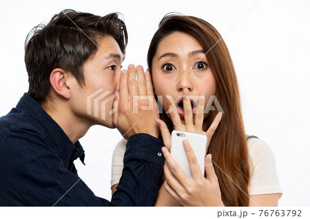 スマートフォン・耳打ちする男性に驚く女性 76763792