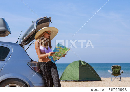 travel to the sea by car. the girl is looking for a road on the map. the car stopped on the beach 76766898