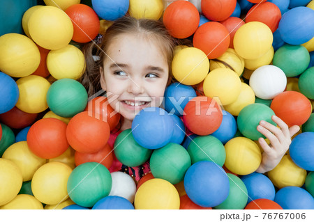 a child in the children's playroom. The girl is having fun among the colorful balls. Dry Pool Party 76767006