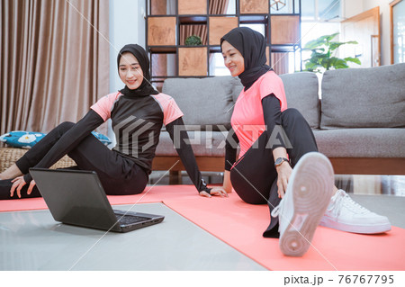 two asian women wearing hijab sportswear sit on the floor while warming up their hips together two asian women wearing hijab sportswear sit on the floor while warming up their hips together 76767795