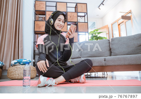 a woman wearing a hijab sportswear wearing earphones and a cellphone while listening to music 76767897