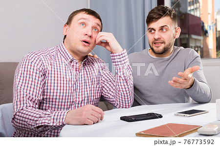 Friend calming distressed guy at home table Friend calming distressed guy at home table 76773592