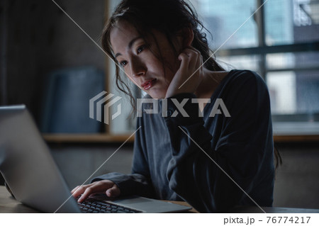 悩みながらパソコンを見つめる女性 76774217