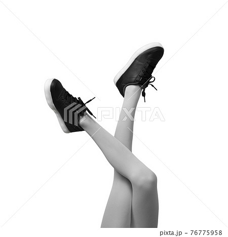 New Black female sneakers on long slender woman legs in light grey tights isolated on white background. New Black female sneakers on long slender woman legs in light grey tights isolated on white background. 76775958