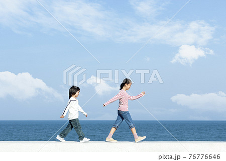 防波堤を歩く女の子と男の子 76776646