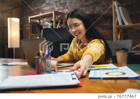 Young woman working in modern office using devices and gadgets. Making reports, analitycs, routine processing tasks Young woman working in modern office using devices and gadgets. Making reports, analitycs, routine processing tasks 76777467