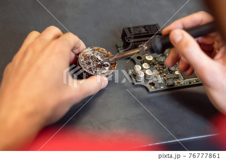 Male hands holding soldering iron near solder Male hands holding soldering iron near solder 76777861