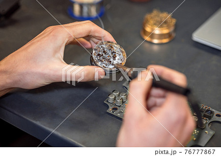 Hands with hot soldering iron touching solder Hands with hot soldering iron touching solder 76777867