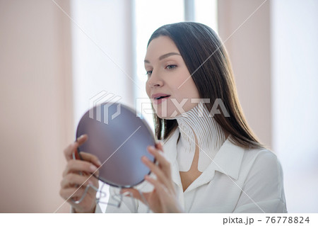 Cute young woman with tapes on her neck looking in the mirror 76778824