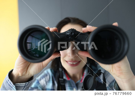 Woman looking through black binoculars and holding it with her hands 76779660