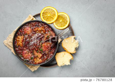 Feijoada in black bowl gray concrete table top. Brazilian and portuguese cuisines beans meat stew Feijoada in black bowl gray concrete table top. Brazilian and portuguese cuisines beans meat stew 76780128