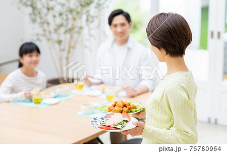 食卓の家族と料理を運ぶ母親の写真素材