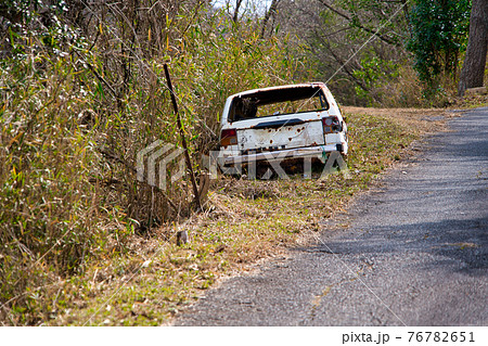 山中の道端に乗り捨てられた自動車 76782651
