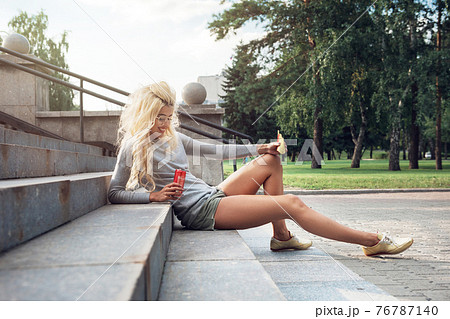 beauty blonde young woman sitting on outdoor and eating 76787140