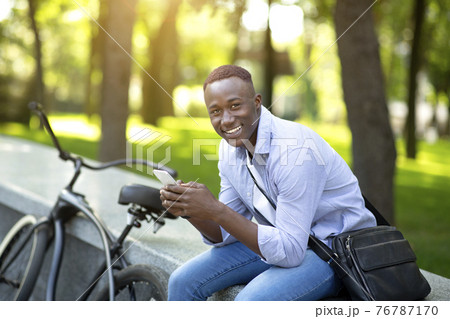 Happy black man with bicycle chatting on smartphone at urban park Happy black man with bicycle chatting on smartphone at urban park 76787170