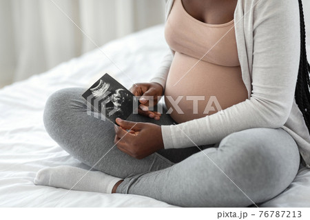 Fetal Development. Pregnant african woman looking at baby ultrasound scan at home Fetal Development. Pregnant african woman looking at baby ultrasound scan at home 76787213