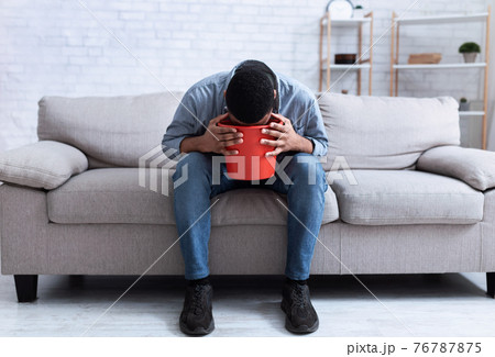 African Man Vomiting Into Bucket Sitting On Couch At Home African Man Vomiting Into Bucket Sitting On Couch At Home 76787875