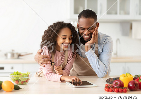 Black man and girl cooking in kitchen using digital tablet Black man and girl cooking in kitchen using digital tablet 76788475